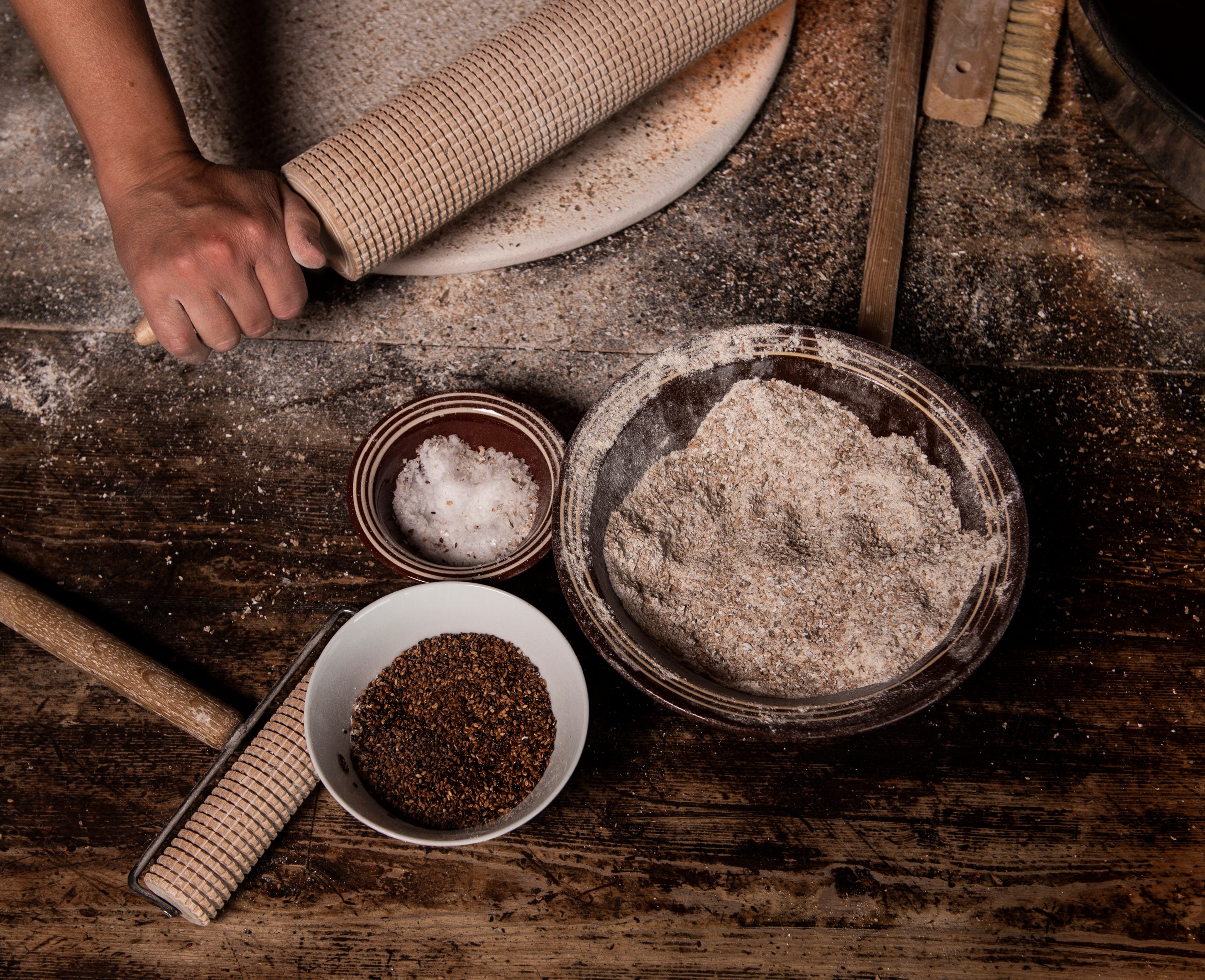 Tradisjonell flatbrødbaking med kjevle, mjøl, salt og frø på rustikt trebord